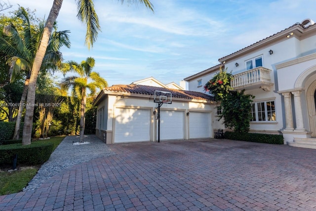 view of front of house with a garage, a balcony, driveway, a tiled roof, and stucco siding