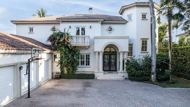 mediterranean / spanish house with a tiled roof, stucco siding, french doors, and a balcony