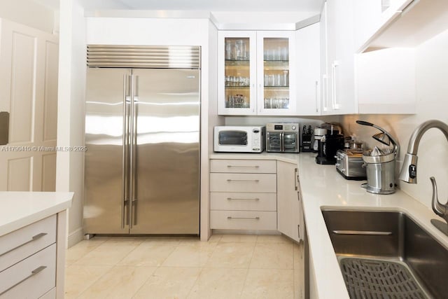 kitchen with built in refrigerator, white microwave, light countertops, and a sink