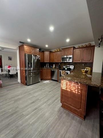 kitchen featuring appliances with stainless steel finishes, dark stone counters, brown cabinets, and light wood-type flooring