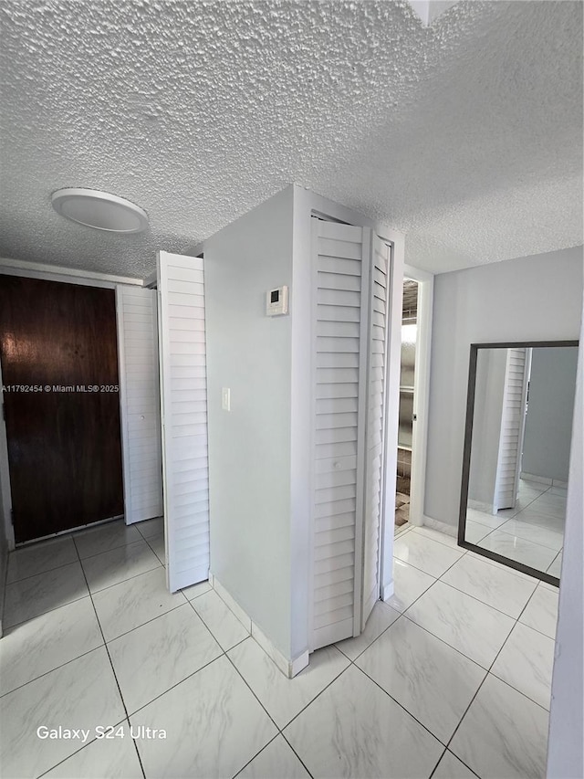 hall featuring a textured ceiling, baseboards, and marble finish floor