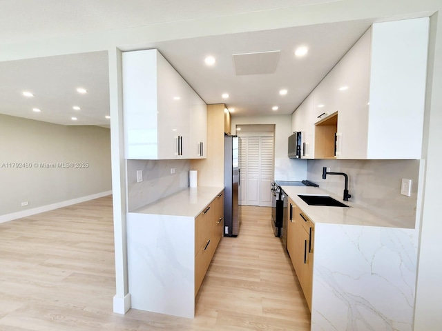kitchen with a sink, light wood-style floors, freestanding refrigerator, range with electric stovetop, and modern cabinets