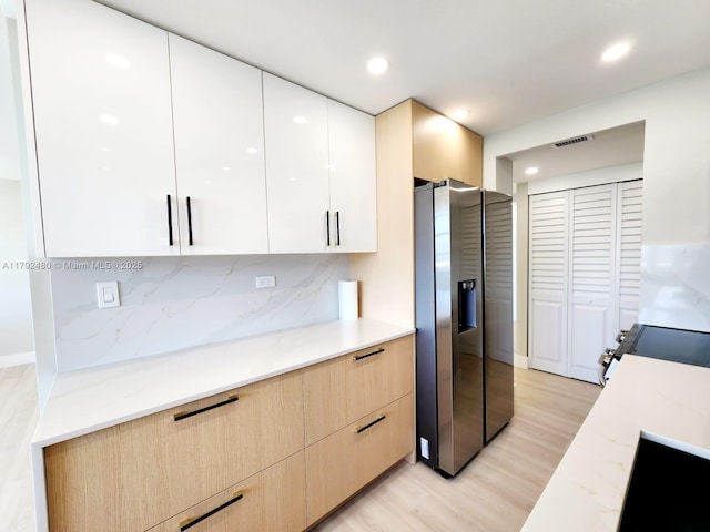 kitchen with modern cabinets, visible vents, light wood-style flooring, light stone counters, and appliances with stainless steel finishes