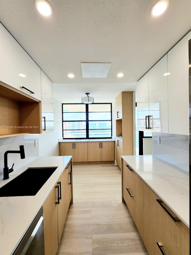 kitchen featuring modern cabinets, a sink, light stone countertops, and light wood-type flooring