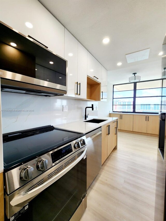 kitchen with modern cabinets, a sink, appliances with stainless steel finishes, and white cabinetry