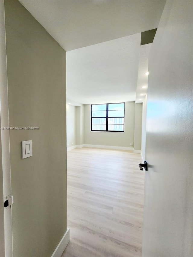 hallway with light wood-type flooring and baseboards