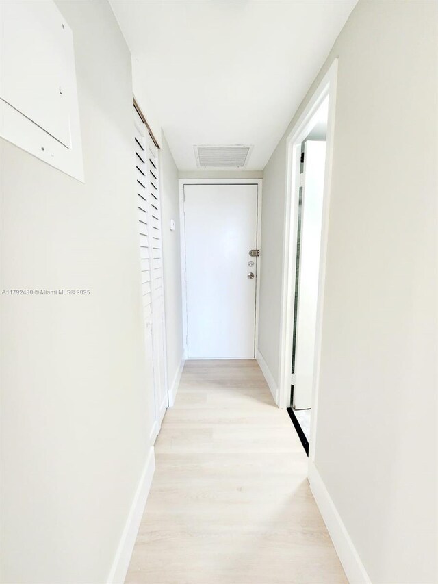 hallway with light wood finished floors, visible vents, and baseboards