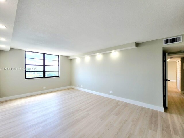 unfurnished room featuring baseboards, visible vents, a textured ceiling, and light wood finished floors