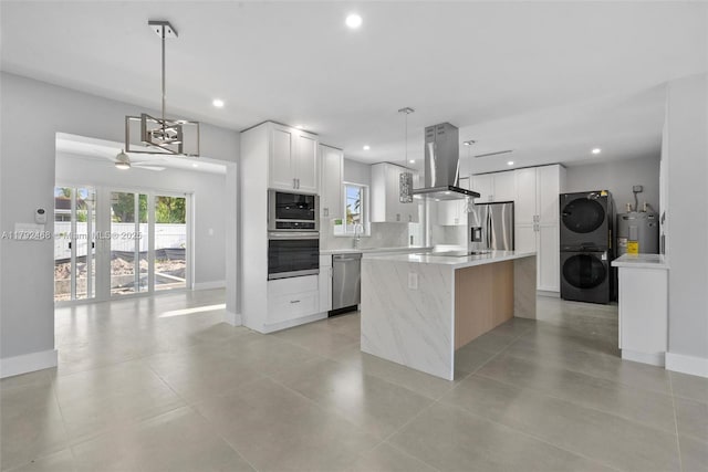 kitchen featuring stacked washer and dryer, light countertops, stainless steel appliances, island exhaust hood, and electric water heater