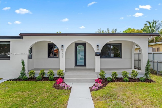 view of exterior entry with a lawn, covered porch, and stucco siding