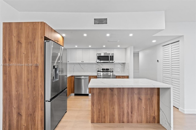 kitchen featuring white cabinets, light wood-style flooring, stainless steel appliances, decorative backsplash, and visible vents