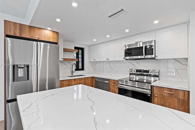 kitchen with brown cabinetry, visible vents, light stone counters, a sink, and appliances with stainless steel finishes