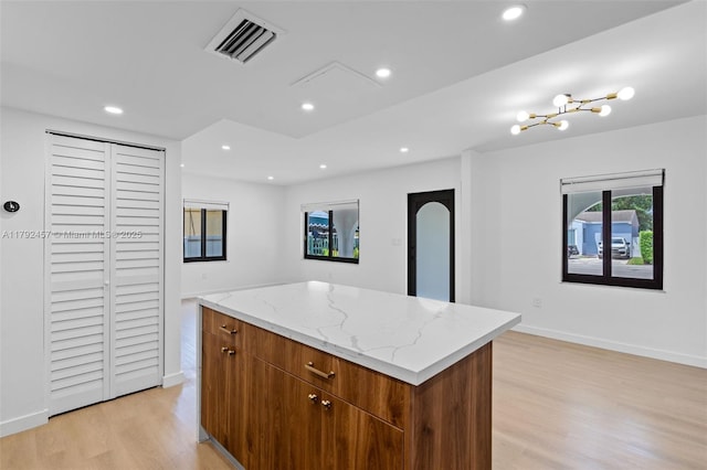 kitchen featuring visible vents, a kitchen island, recessed lighting, light stone counters, and light wood finished floors