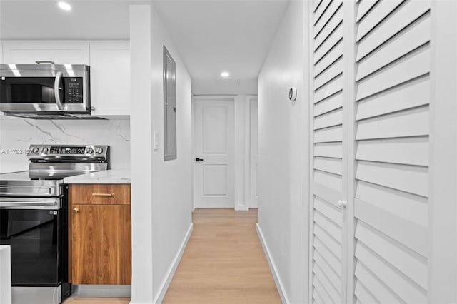 hall featuring recessed lighting, baseboards, electric panel, and light wood-style floors