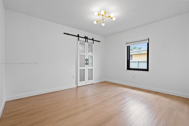 spare room featuring light wood-style floors, a barn door, baseboards, and a notable chandelier