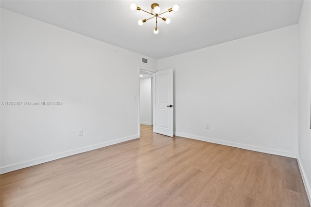 empty room with an inviting chandelier, light wood finished floors, baseboards, and visible vents