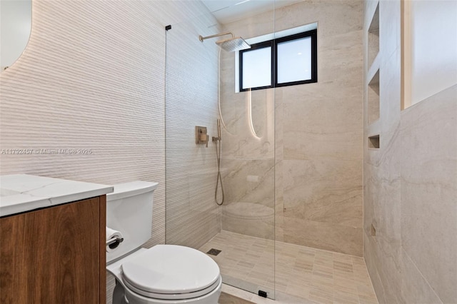 full bathroom with vanity, toilet, tiled shower, and tile walls