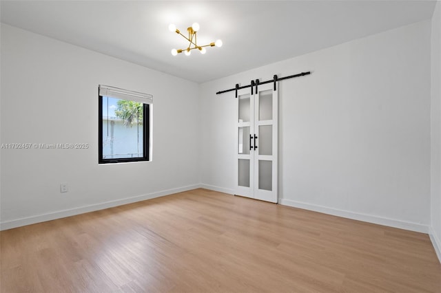spare room featuring light wood-type flooring, a barn door, baseboards, and a notable chandelier