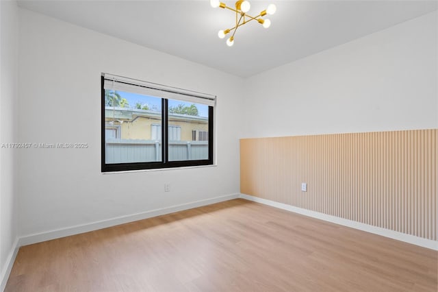 spare room featuring baseboards, a chandelier, and wood finished floors