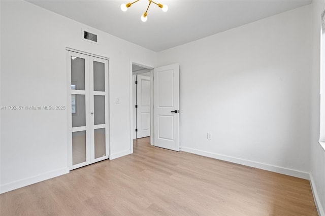 unfurnished bedroom featuring light wood-style floors, an inviting chandelier, and visible vents