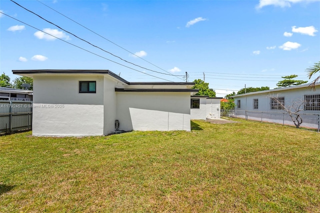 back of house featuring a lawn, fence, and stucco siding