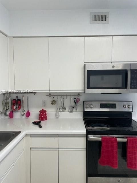 5161 Collins Ave Unit 506, Miami Beach, FL 33140 - kitchen with a sink, stainless steel appliances, visible vents, white cabinetry, and light countertops