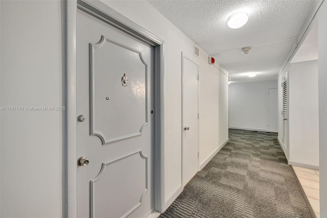 hallway featuring a textured ceiling, visible vents, baseboards, and carpet