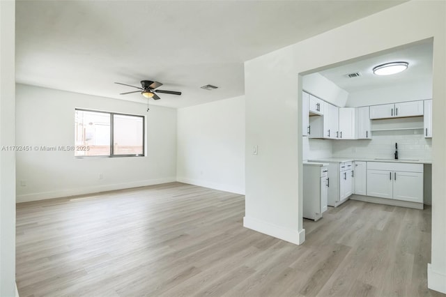 unfurnished living room with baseboards, ceiling fan, a sink, and light wood-style floors