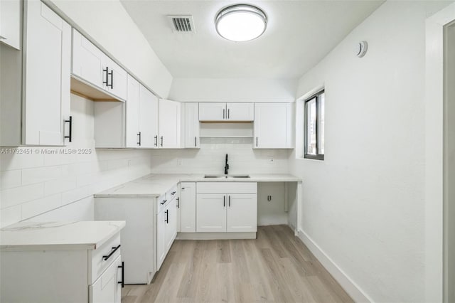kitchen with visible vents, white cabinets, a sink, light wood finished floors, and backsplash
