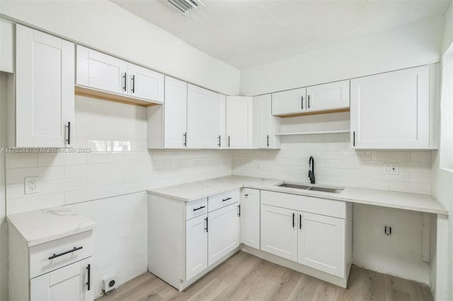 kitchen featuring light stone counters, tasteful backsplash, a sink, light wood-type flooring, and visible vents
