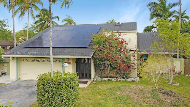 view of front facade with roof mounted solar panels, a shingled roof, a front lawn, and stucco siding