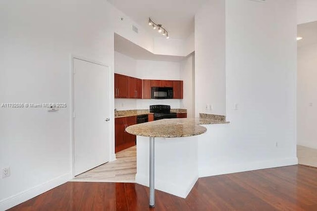 7280 SW 90th St Unit 703, Miami, FL 33156 - kitchen with track lighting, a peninsula, light stone countertops, light wood-type flooring, and black appliances