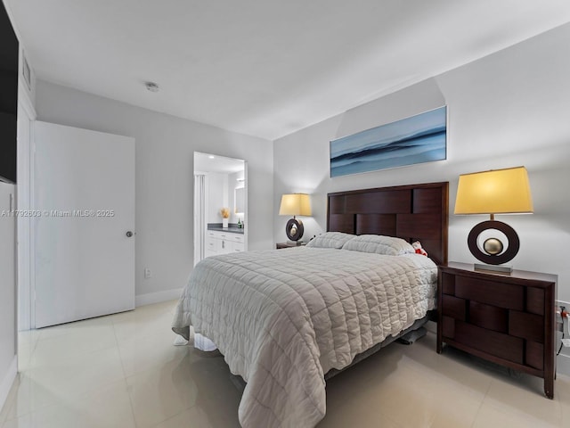 bedroom with baseboards, light tile patterned floors, and ensuite bath