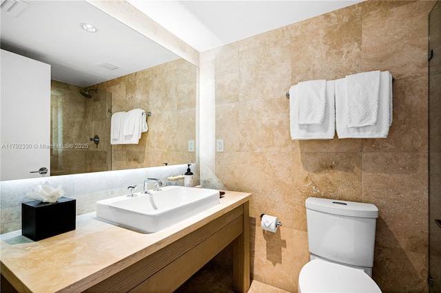 bathroom featuring vanity, toilet, tiled shower, and tile walls