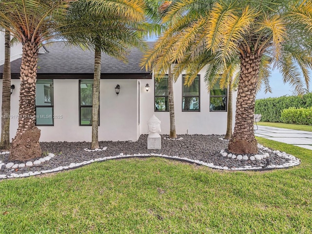 property entrance featuring a lawn, a shingled roof, and stucco siding