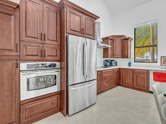 kitchen with brown cabinetry, light countertops, lofted ceiling, stainless steel appliances, and wall chimney exhaust hood