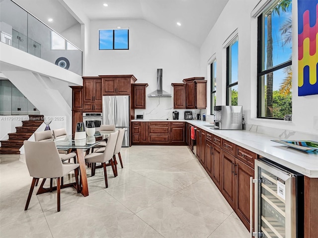 kitchen featuring wall chimney range hood, light countertops, beverage cooler, high vaulted ceiling, and stainless steel appliances