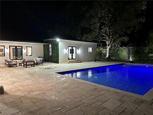 pool at twilight with a patio area, an outdoor pool, french doors, and an outdoor hangout area