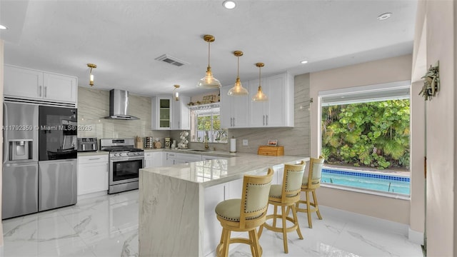 kitchen with decorative backsplash, marble finish floor, wall chimney range hood, a sink, and stainless steel appliances