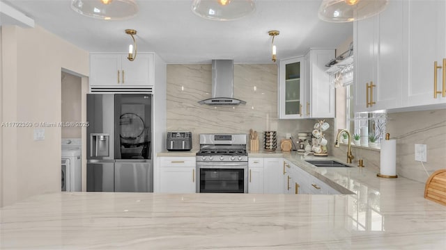 kitchen featuring wall chimney range hood, backsplash, light stone countertops, a sink, and stainless steel appliances