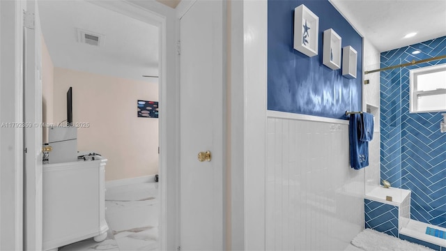 bathroom featuring visible vents, wainscoting, tiled shower, and marble finish floor