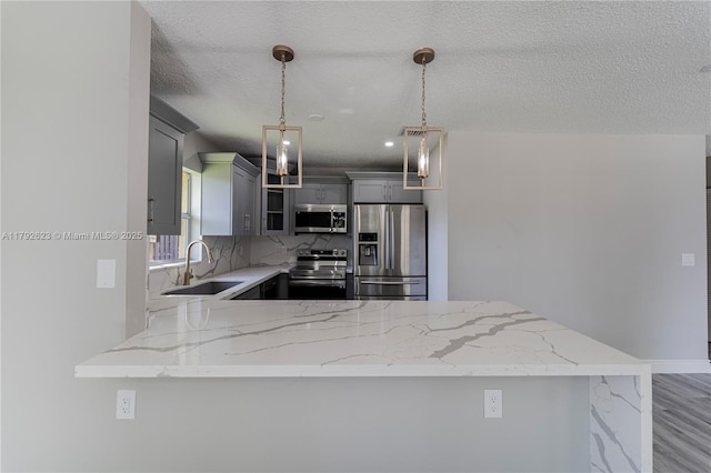 kitchen with a sink, appliances with stainless steel finishes, a peninsula, and light stone counters