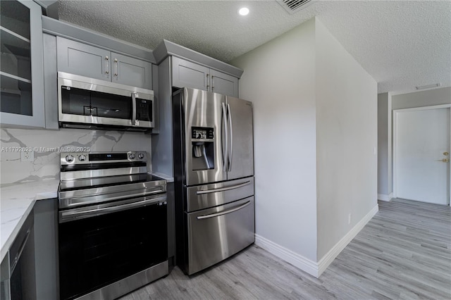 kitchen with light stone countertops, appliances with stainless steel finishes, a textured ceiling, gray cabinets, and light wood-type flooring