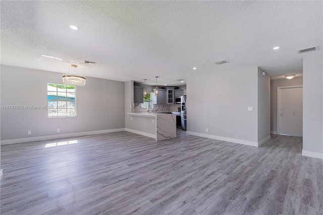 unfurnished living room with a notable chandelier, light wood-style floors, a textured ceiling, baseboards, and visible vents