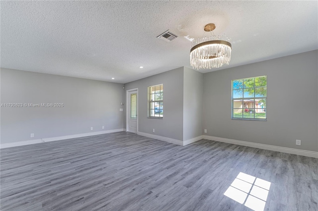 empty room with an inviting chandelier, a textured ceiling, plenty of natural light, and wood finished floors