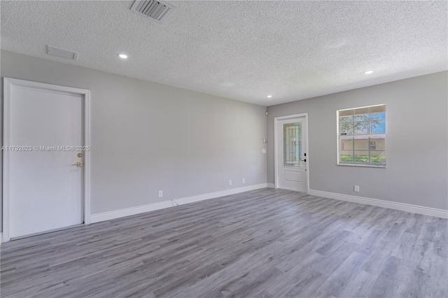 empty room with a textured ceiling, wood finished floors, and visible vents