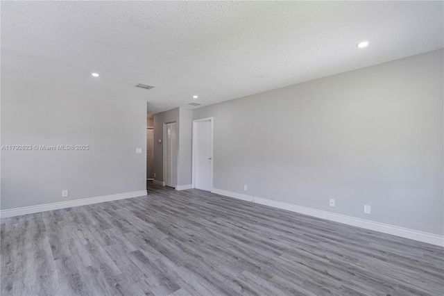 empty room with baseboards, a textured ceiling, recessed lighting, and wood finished floors