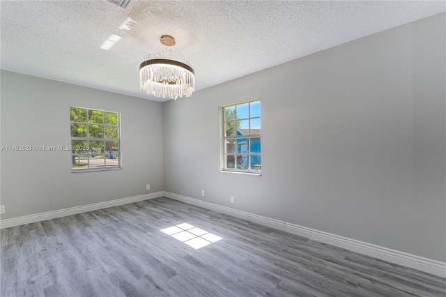 spare room featuring baseboards, a textured ceiling, a notable chandelier, and wood finished floors