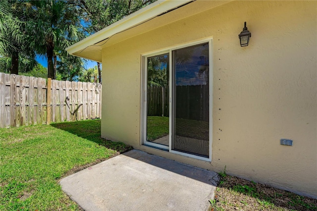 doorway to property featuring fence, stucco siding, a lawn, and a patio area
