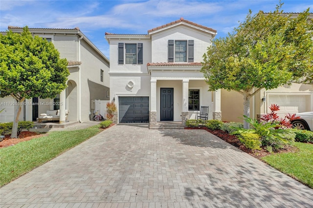 mediterranean / spanish home featuring an attached garage, decorative driveway, stucco siding, a porch, and a tile roof